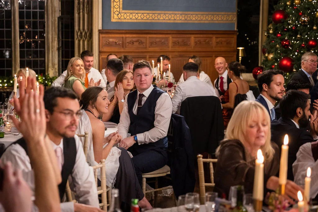Wedding guests enjoy a candlelit wedding breakfast in a stately wood-panelled dining room decorated for Christmas with a large decorated tree.