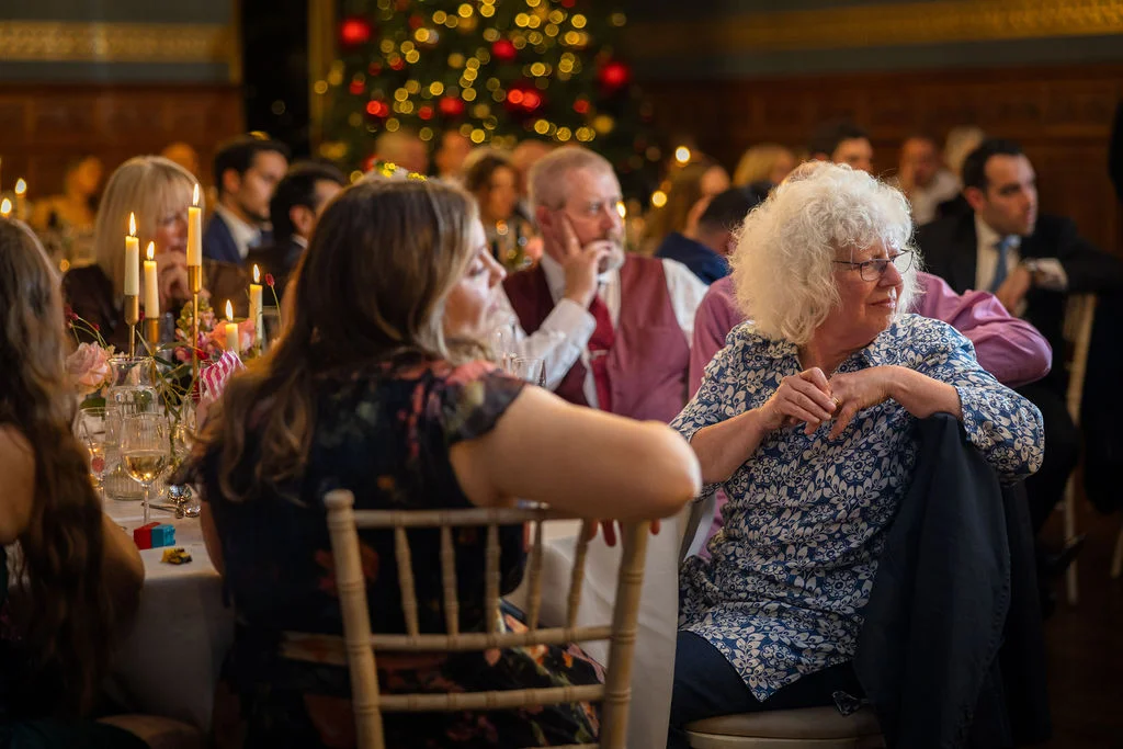 Guests enjoy a warm and festive wedding breakfast seated at candlelit tables with a glowing Christmas tree in the background.