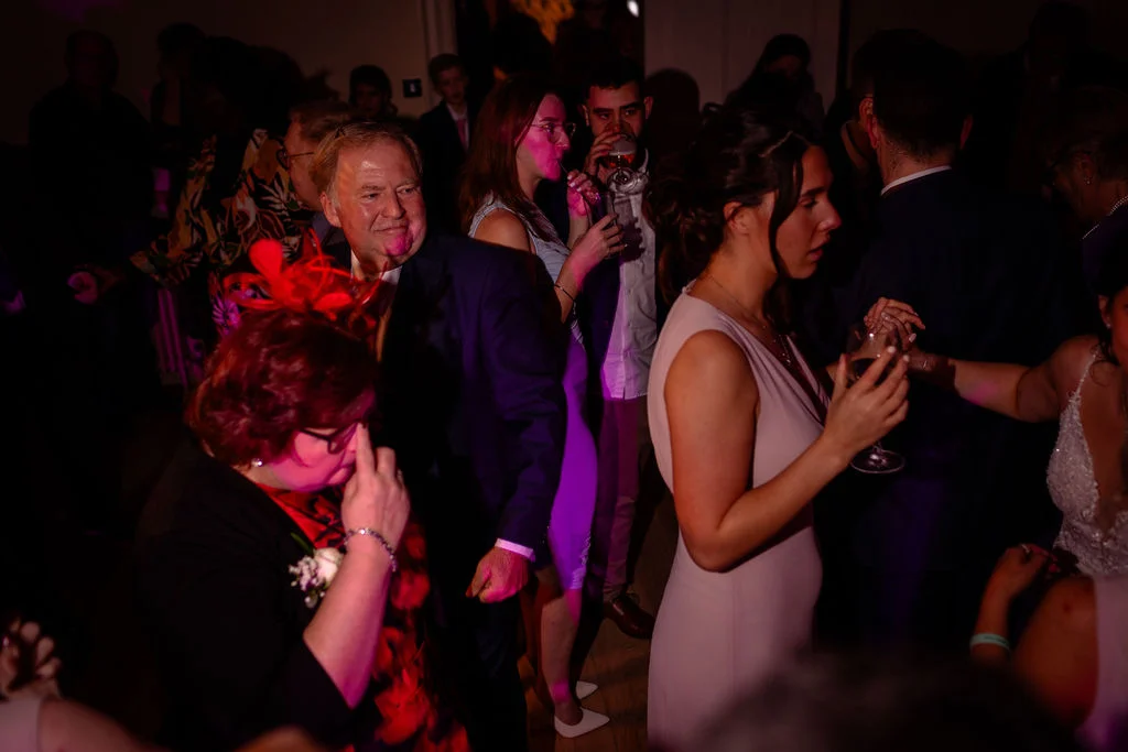 Wedding guests enjoy the evening reception, mingling and dancing under ambient pink lighting.
