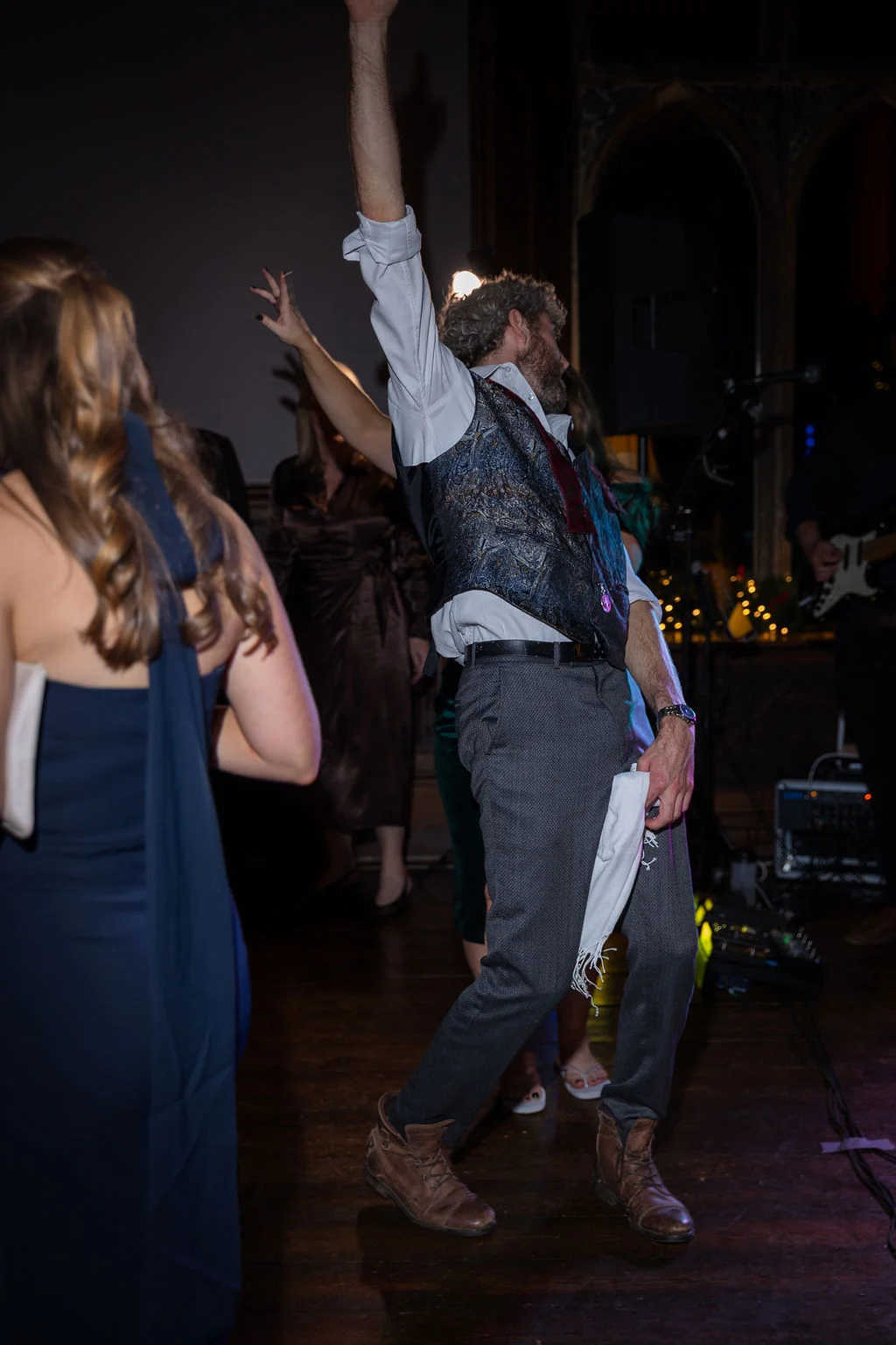 A guest dances enthusiastically with one arm raised high on the dimly lit evening dance floor during a wedding reception.