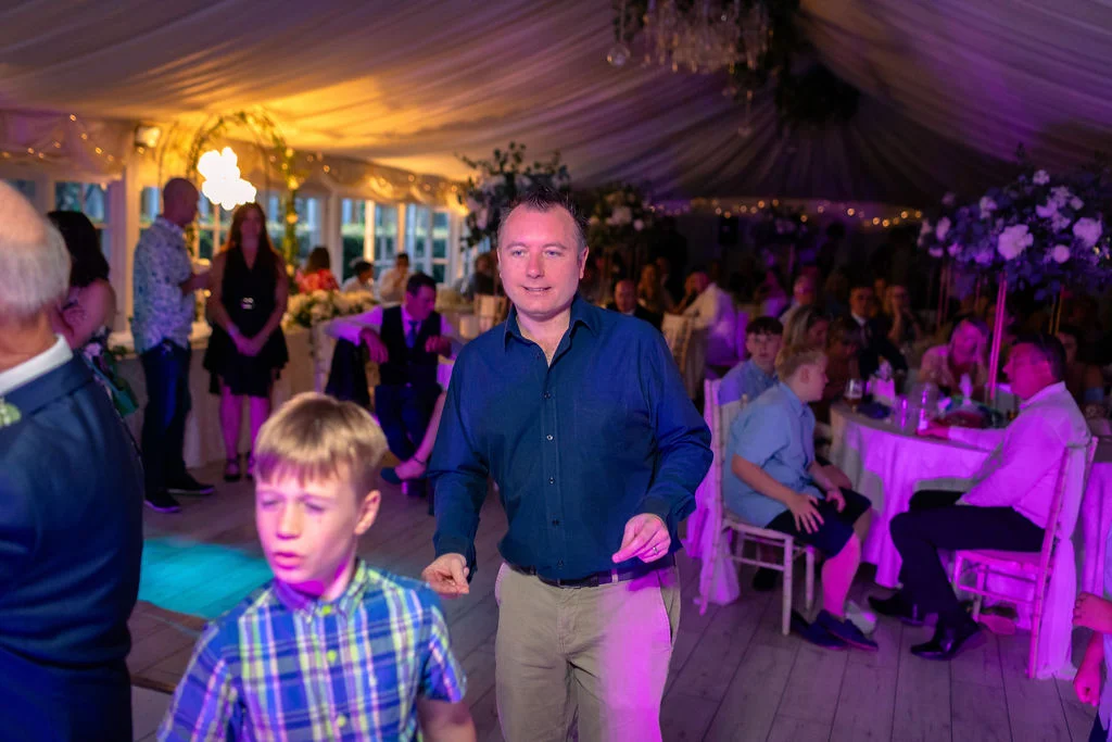 Guests enjoy themselves on the dance floor under a draped marquee illuminated with purple and warm lighting.