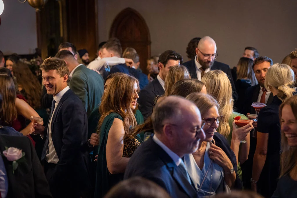 A bustling room of wedding guests mingle and laugh happily together during a lively drinks reception.