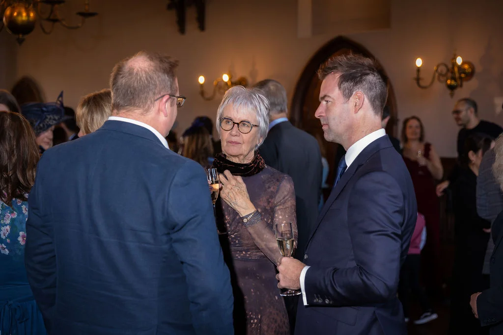 Wedding guests mingling and chatting while holding champagne flutes during the drinks reception in a traditional venue.