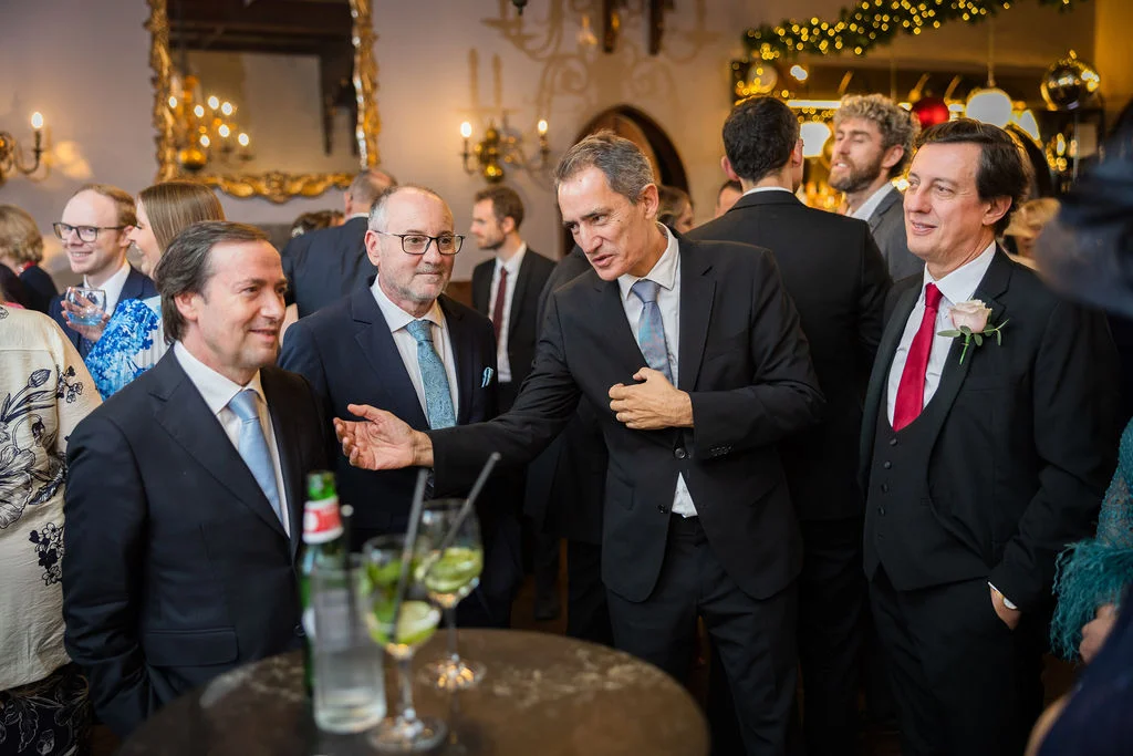 A candid photograph of wedding guests mingling and chatting animatedly during a lively drinks reception inside an elegant venue.