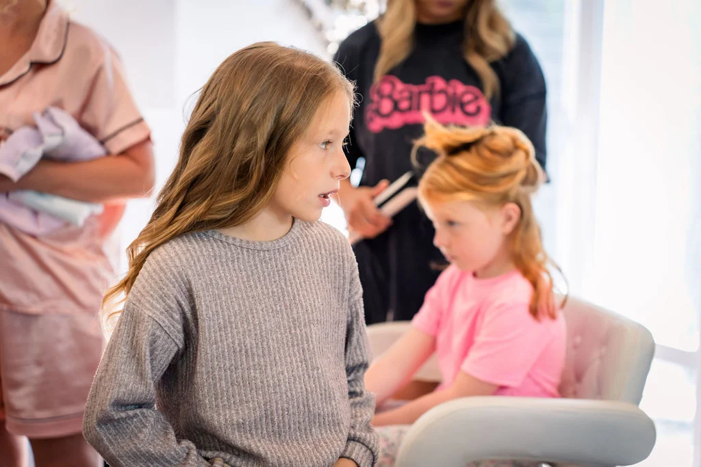 Young children are captured in a candid moment during wedding morning preparations while wearing casual clothing indoors.