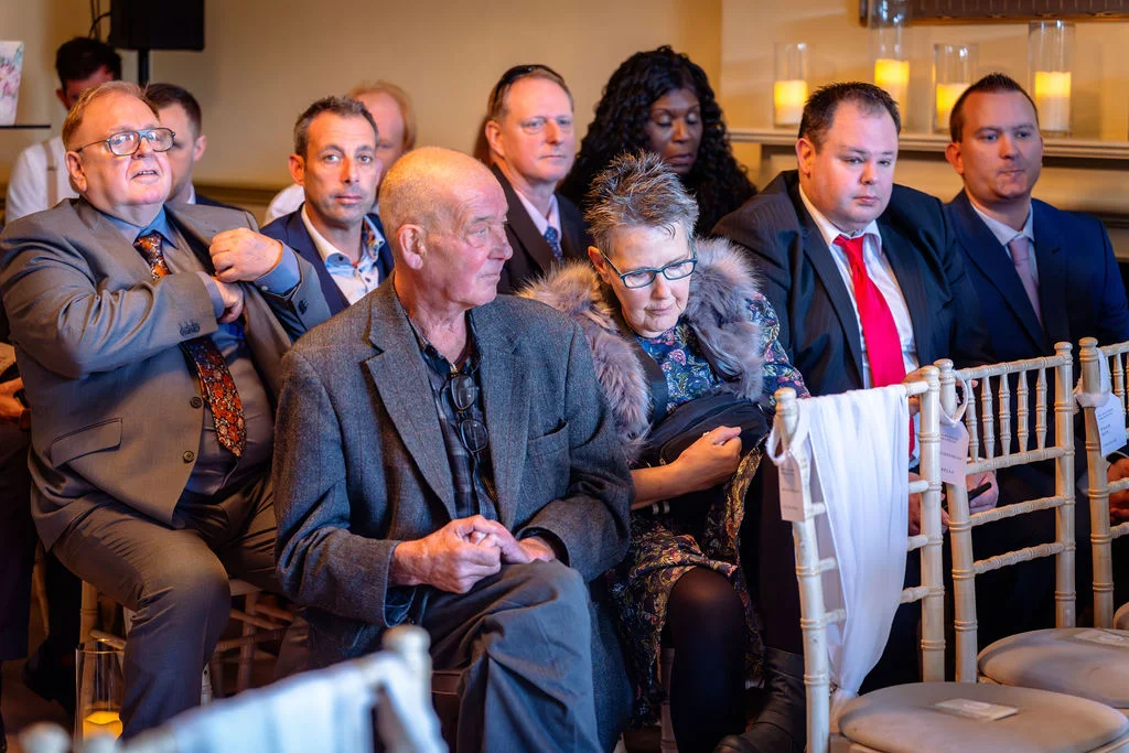 A candid group of wedding guests seated and watching the ceremony with engaged expressions indoors.