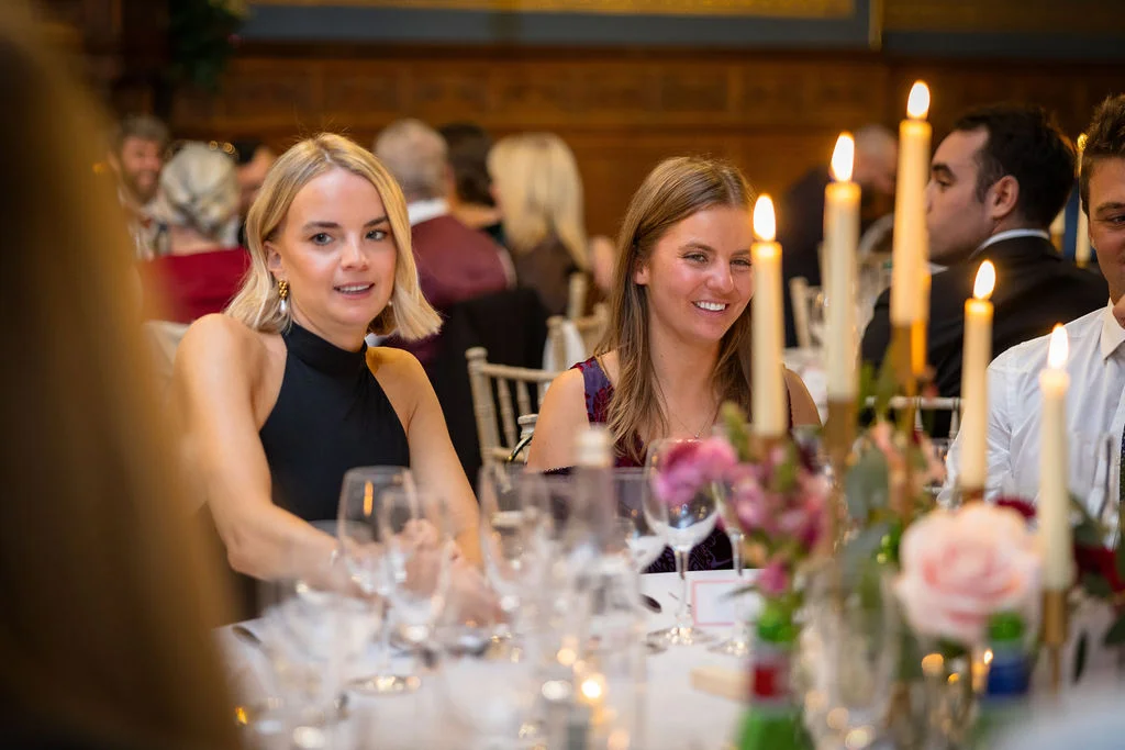 Wedding guests smiling and mingling around a candlelit round banquet table during the wedding reception.