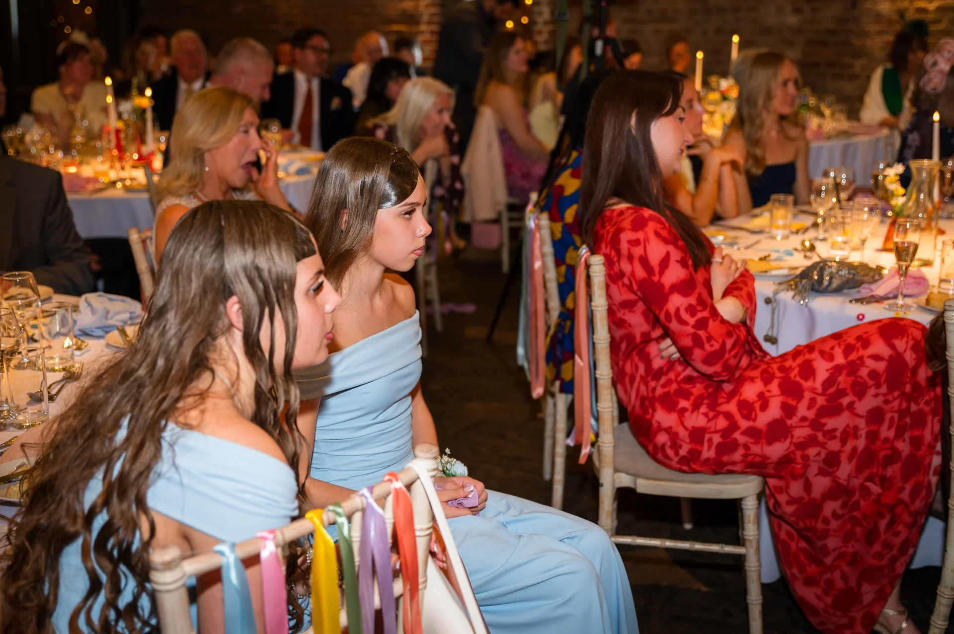 Wedding guests seated at round banquet tables inside a candlelit venue with exposed brick walls during the wedding breakfast.