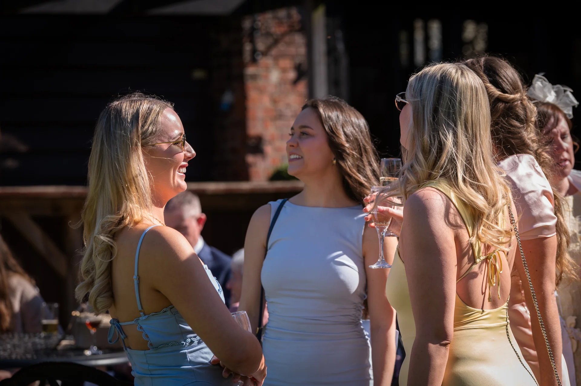 Wedding guests enjoy chatting and holding champagne glasses outdoors during a sunny drinks reception.