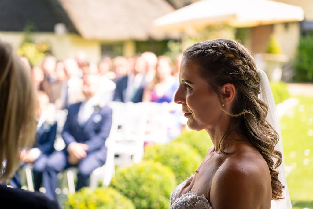 A profile shot of a bride with a braided half-up hairstyle and a strapless lace wedding dress during an outdoor ceremony.