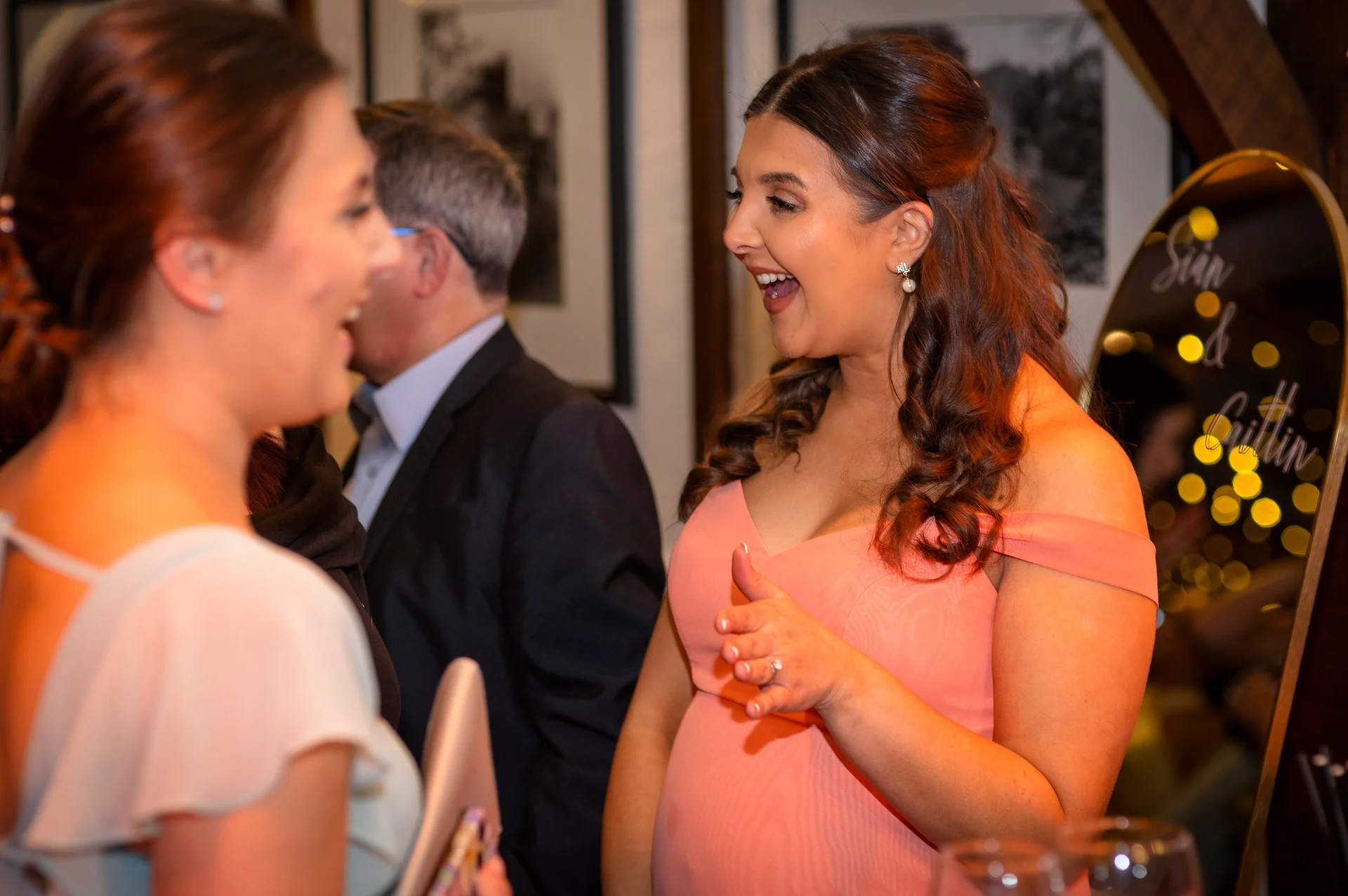 A guest in an off-the-shoulder pink dress laughs heartily while chatting with another wedding attendee during the evening reception.