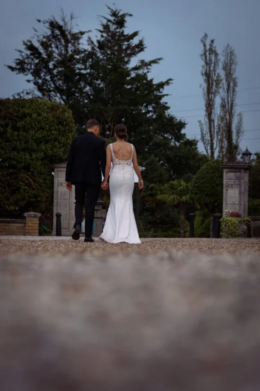 A bride and groom walking down a path at dusk.