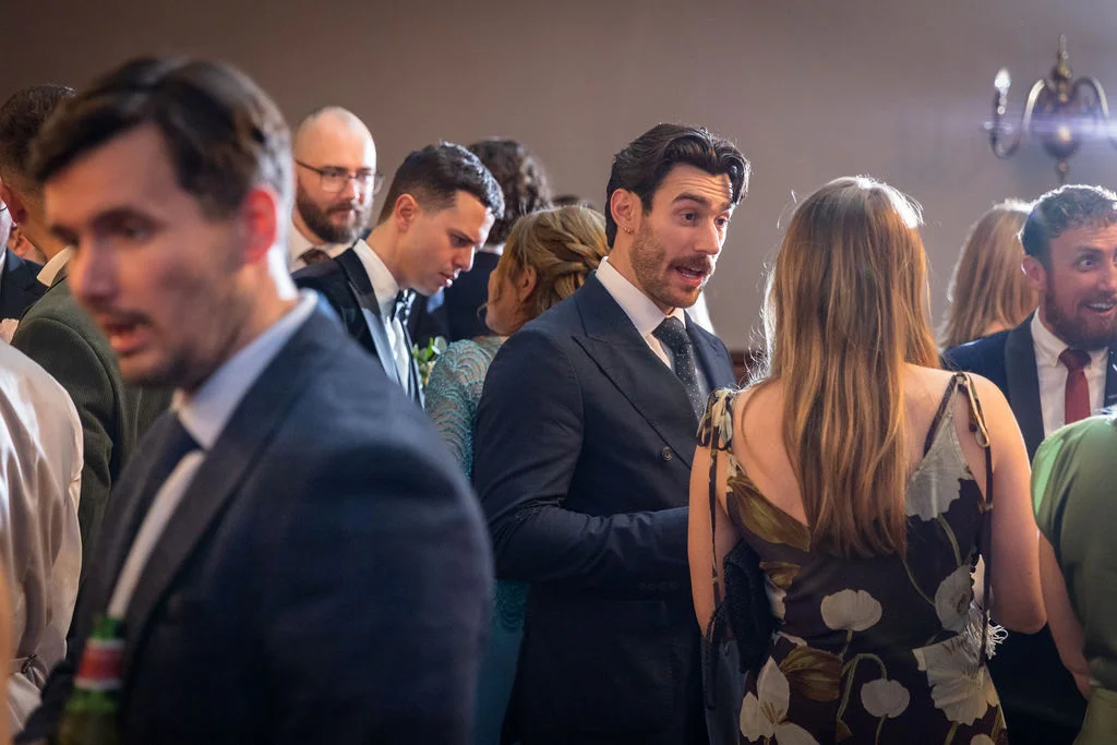 A candid shot of wedding guests mingling and chatting indoors during the reception, captured in natural light.