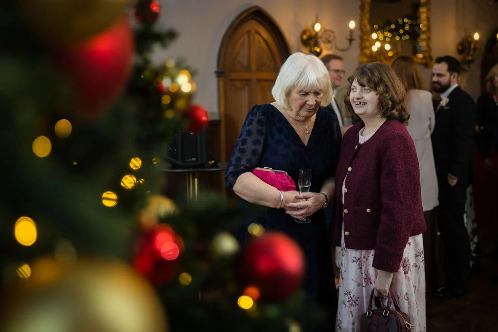 Wedding guests mingling during a festive winter reception near a decorated Christmas tree adorned with red and gold baubles.