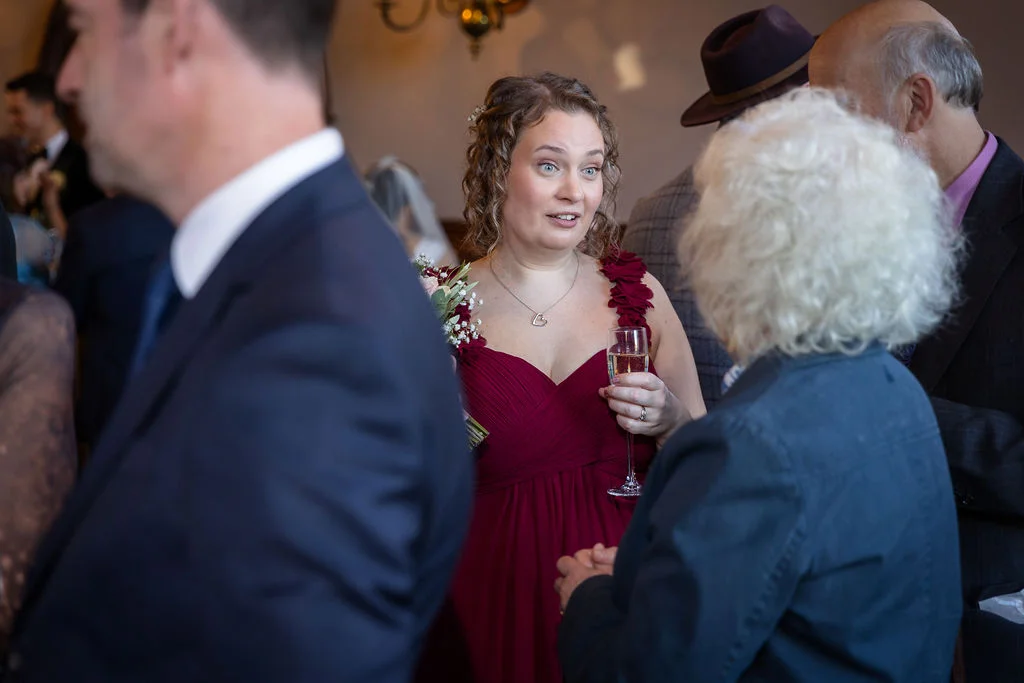 A bridesmaid wearing a deep red gown holding a glass of champagne while mingling with guests at a wedding reception.