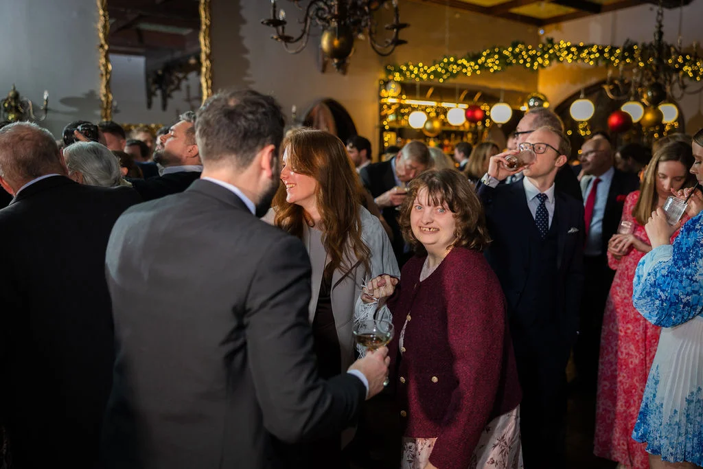 Wedding guests mingle and enjoy drinks during a lively evening reception in a warmly lit, festive venue.