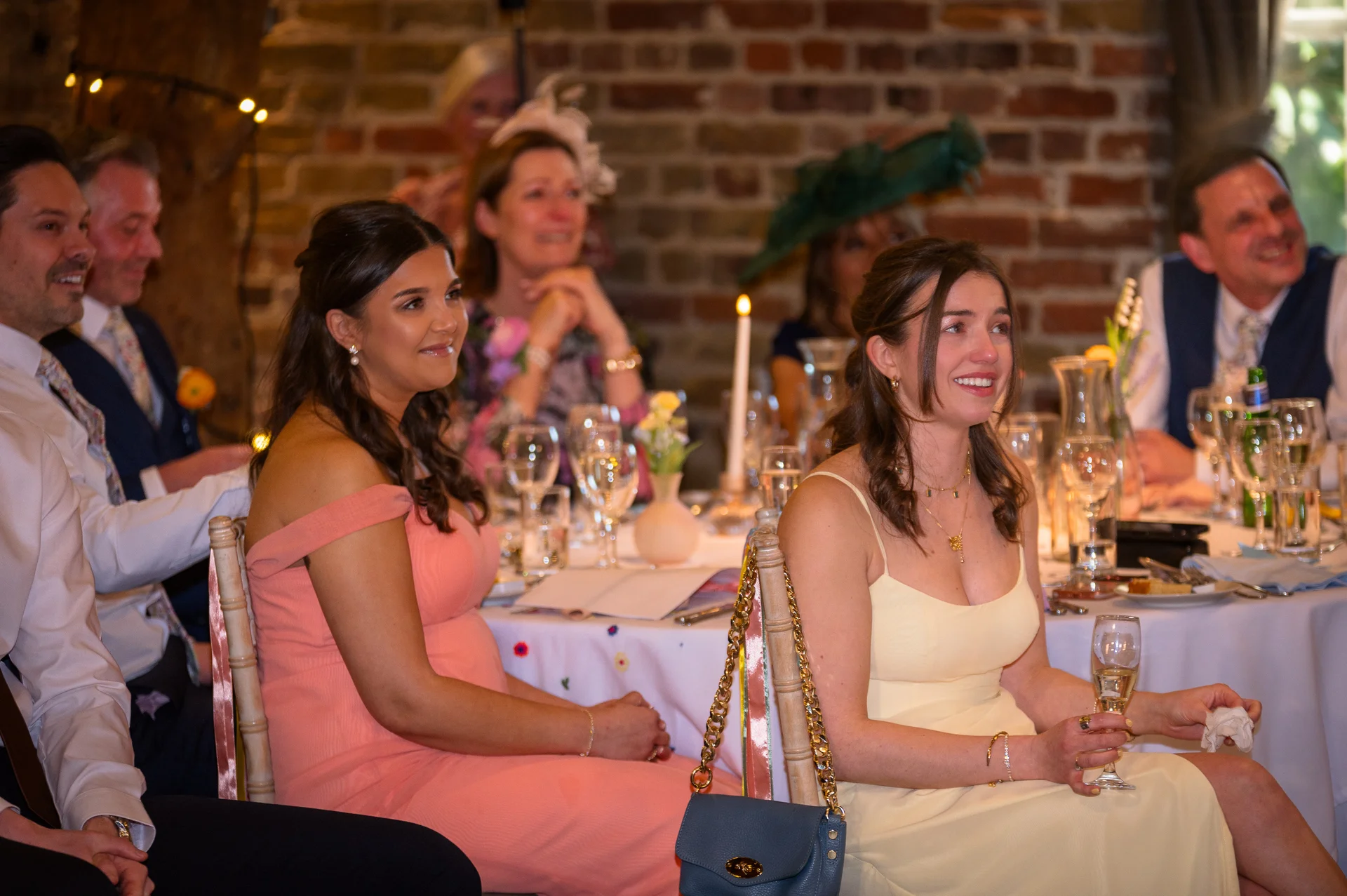 Wedding guests seated at banquet tables in a rustic brick barn laughing and smiling during the wedding speeches.