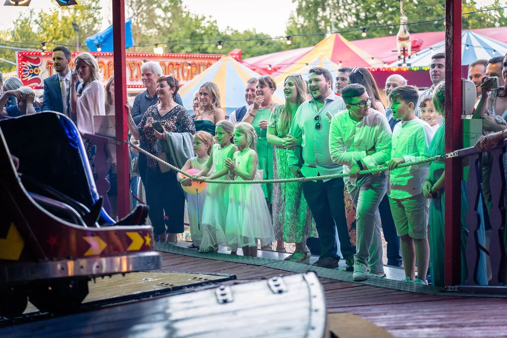 Wedding guests and children gather around a colourful fairground attraction at a festival-themed wedding celebration.