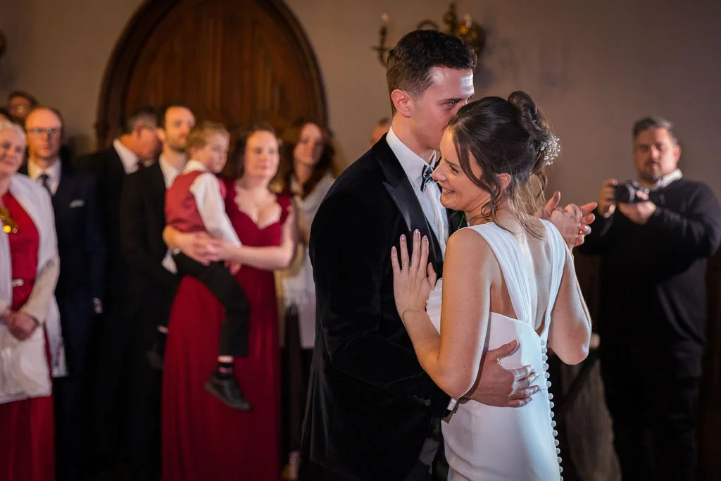 A newlywed couple shares a joyful first dance together as guests look on admiringly in an indoor venue.