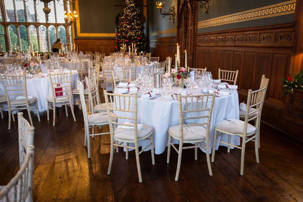 An elegant round wedding table set for a winter banquet in a wood-panelled stately home featuring a decorated Christmas tree in the background.