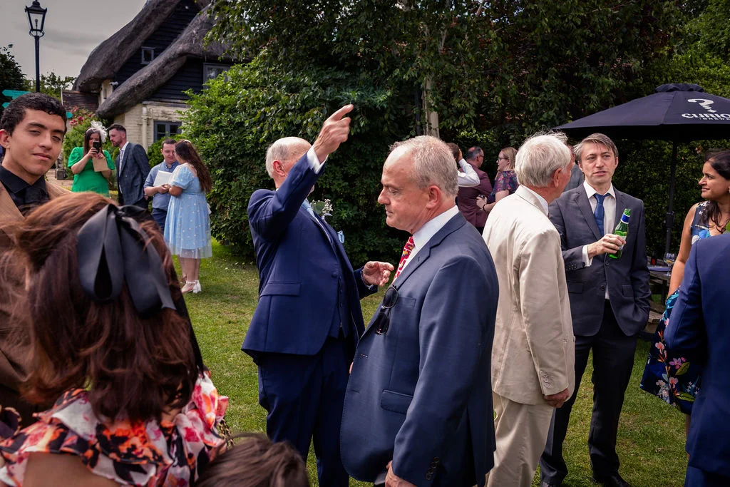 A group of wedding guests mingle and converse outdoors on the lawn during a sunny drinks reception.