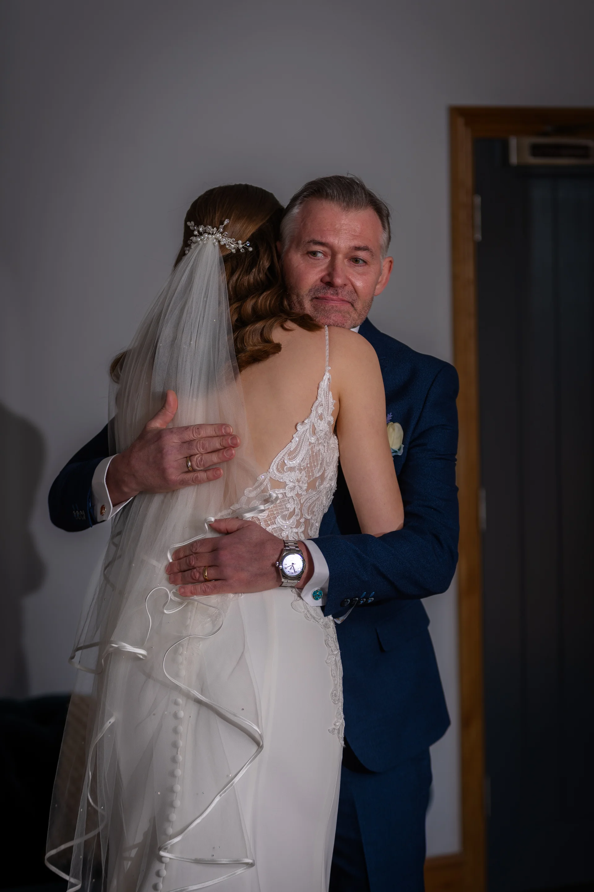 A tearful father embraces his daughter in an emotional moment as she wears a lace-detailed wedding dress and veil.