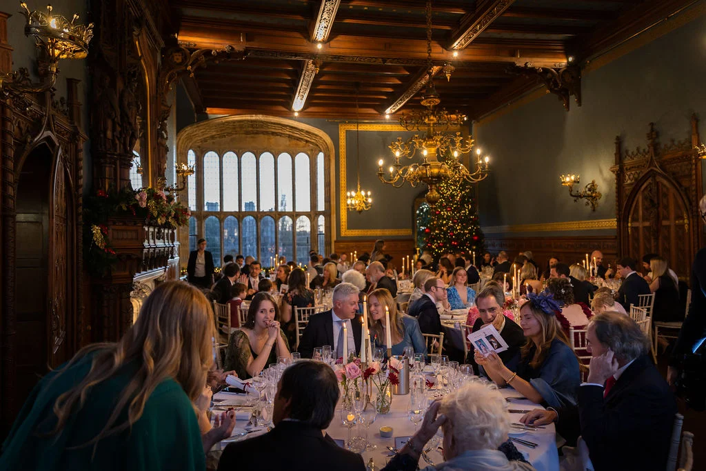 Guests enjoy a candlelit wedding breakfast in a grand, wood-panelled banquet hall adorned with festive Christmas decorations and warm chandeliers.