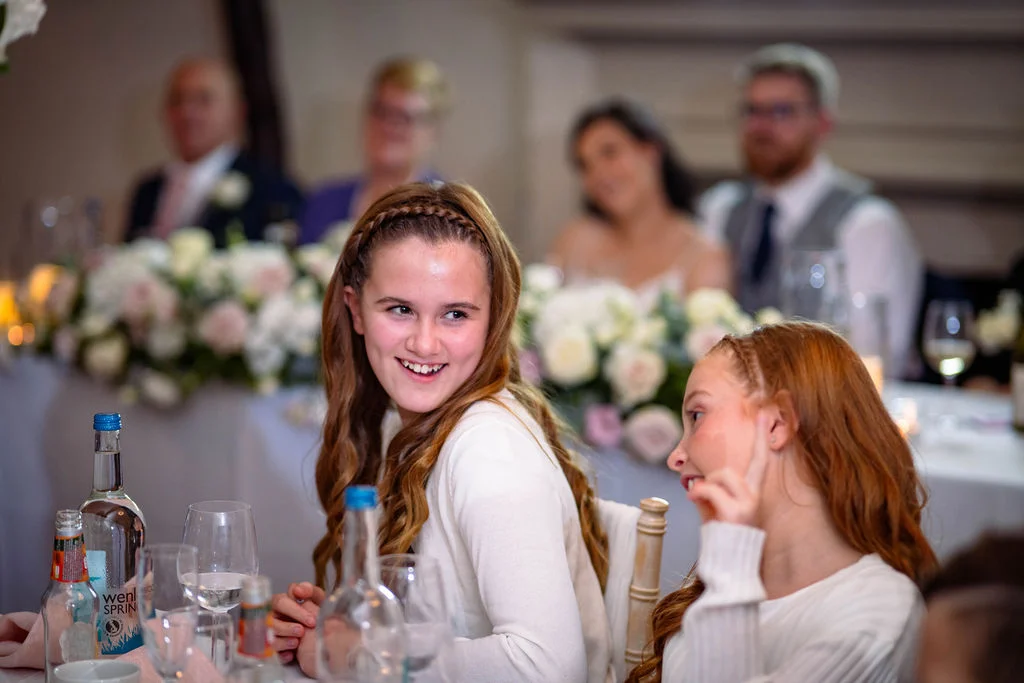 Two young wedding guests smile and chat at a beautifully decorated reception table during the wedding breakfast.