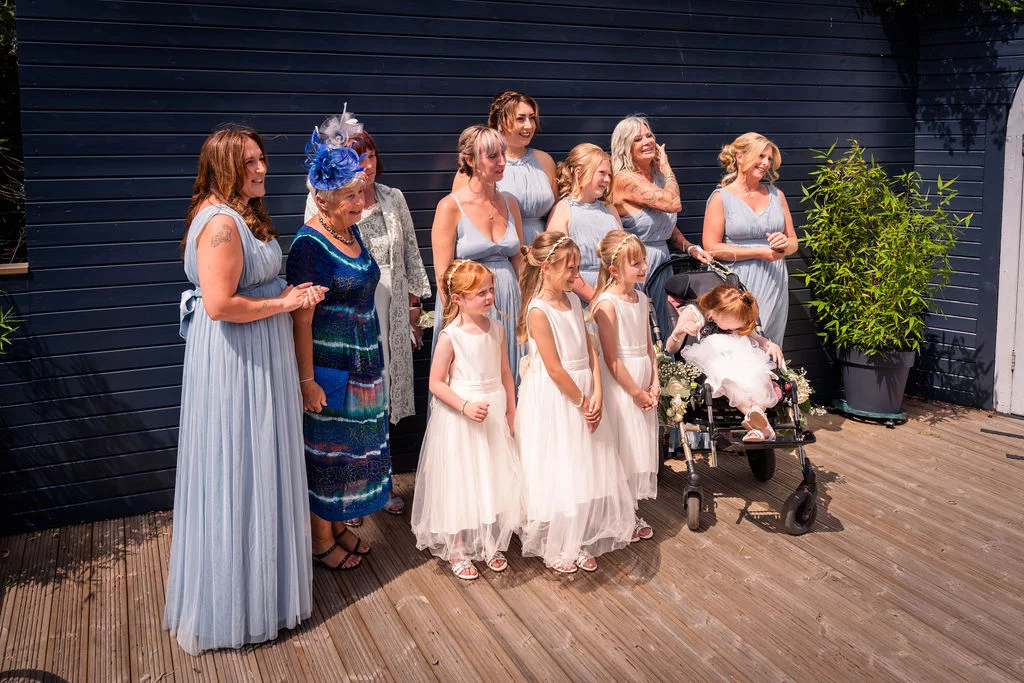A group of wedding guests and family members in blue and white attire gather outdoors on a wooden deck for a portrait.