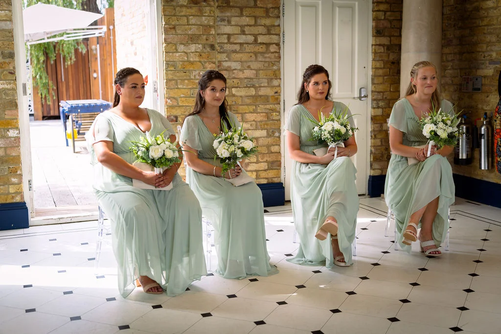 Bridesmaids sitting in a room holding bouquets.