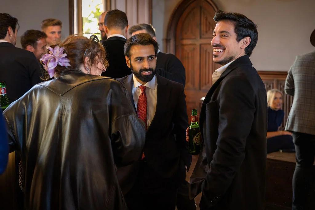 Wedding guests mingle and chat happily together during a drinks reception inside a venue with wooden archways.