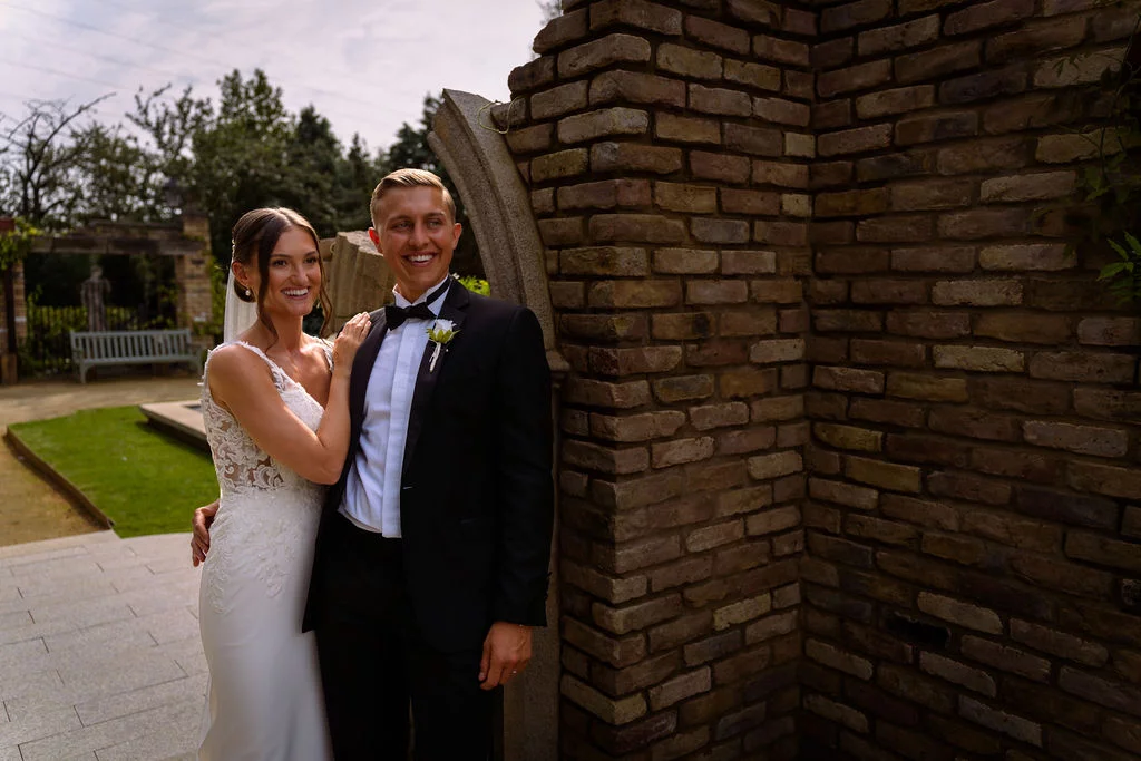 A bride and groom posing in front of a brick wall.