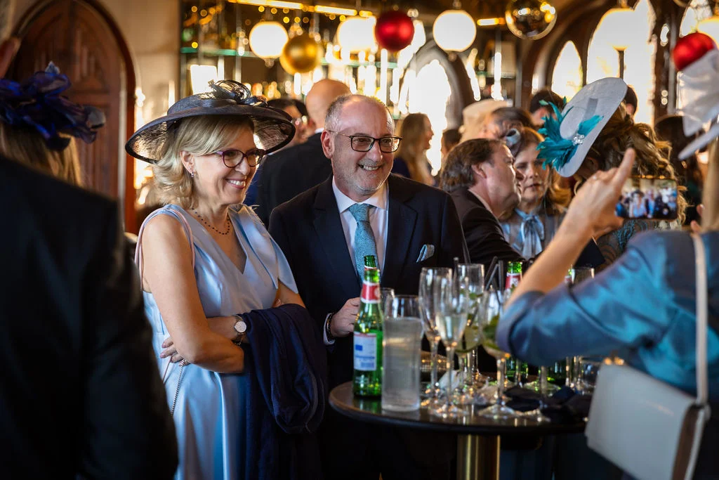 A mature couple smiling and mingling during a wedding drinks reception inside a pub adorned with festive decorations.