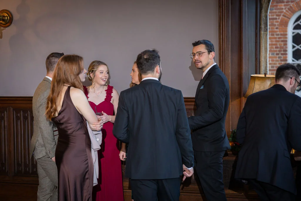 A group of wedding guests mingle and chat during the drinks reception inside an elegant wood-panelled room.