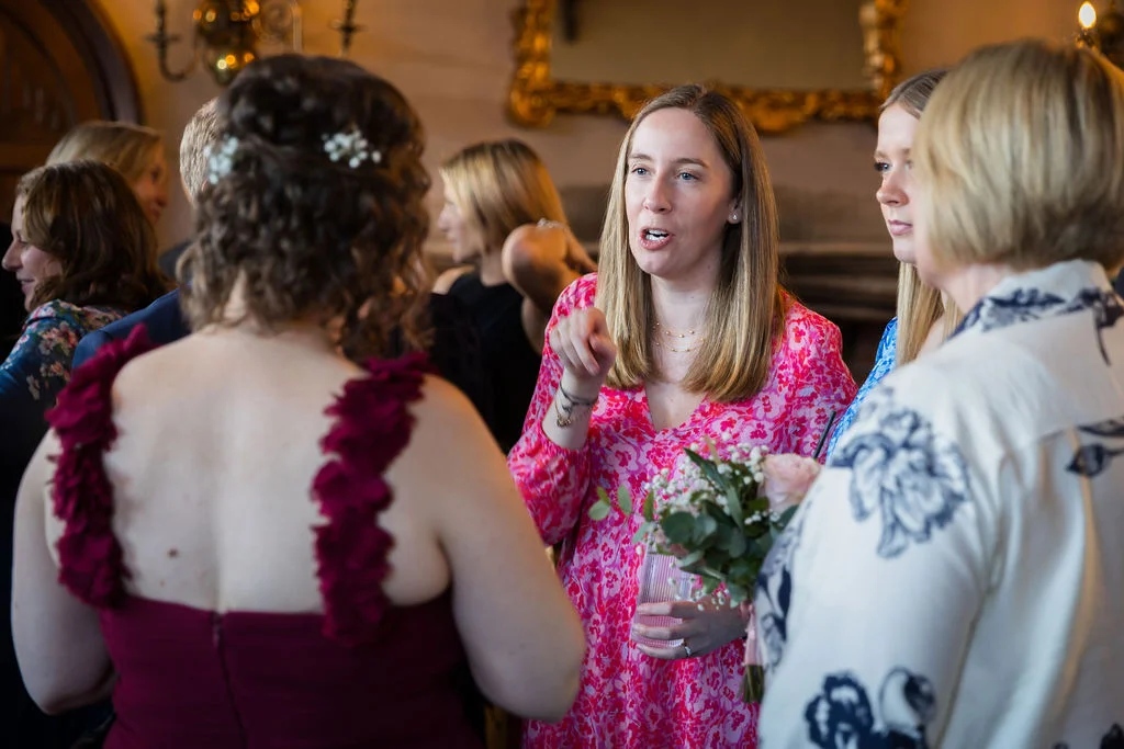 A group of wedding guests mingle and converse naturally indoors during a lively drinks reception.