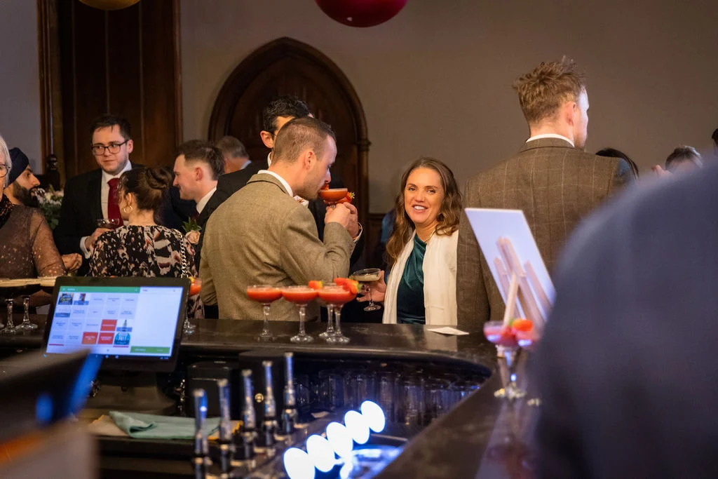 Wedding guests mingle and enjoy cocktails at a lively indoor bar during the evening reception.