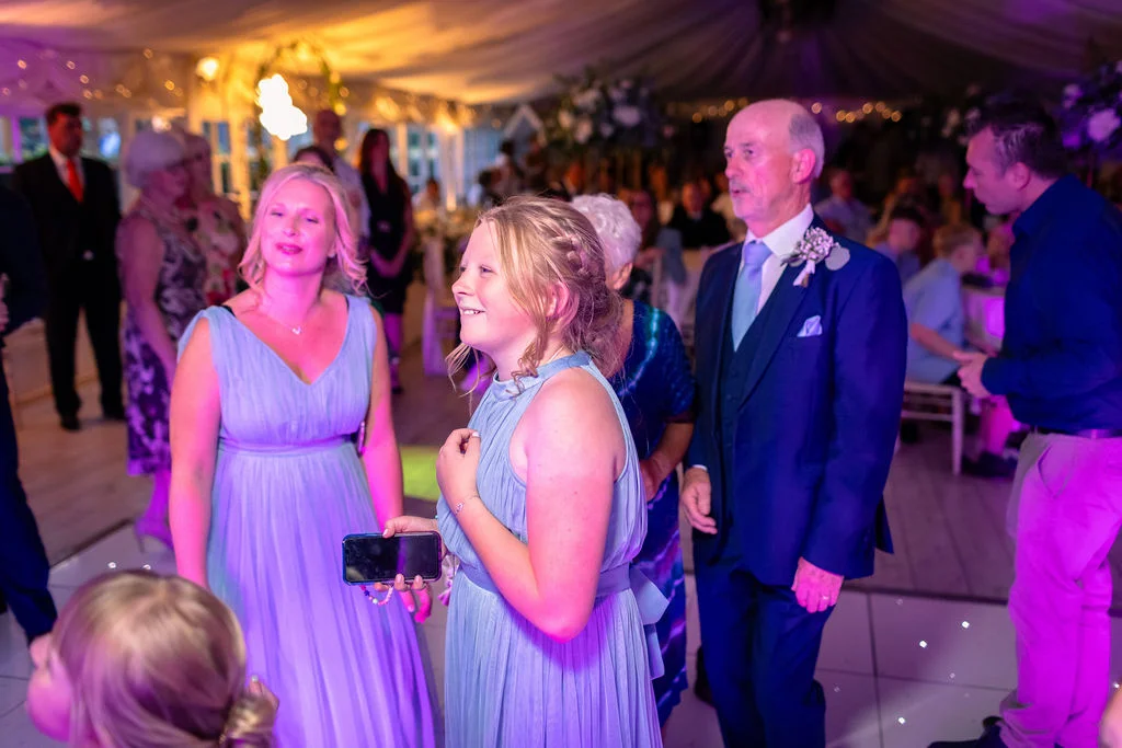 Guests and family members enjoy the evening reception inside a brightly lit marquee, sharing a joyful moment together.