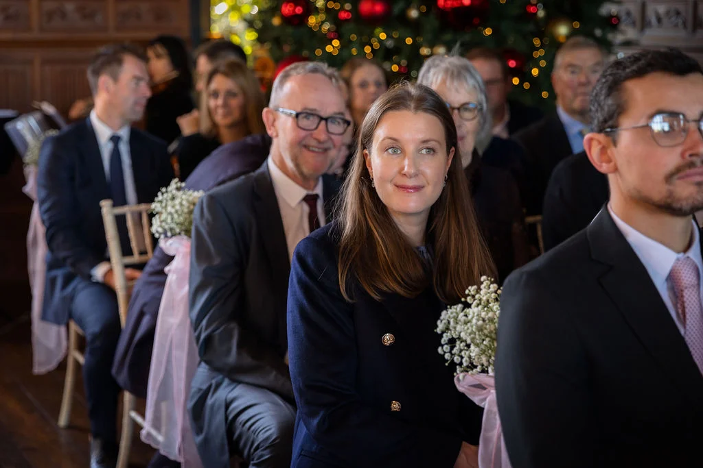 A candid shot of wedding guests seated during a winter ceremony decorated with fairy lights and baby's breath floral chair accents.