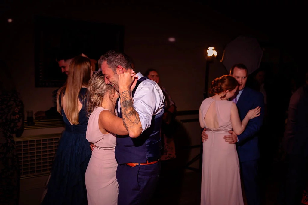 Wedding guests enjoy dancing on the dimly lit evening reception dance floor, captured with a direct flash style.