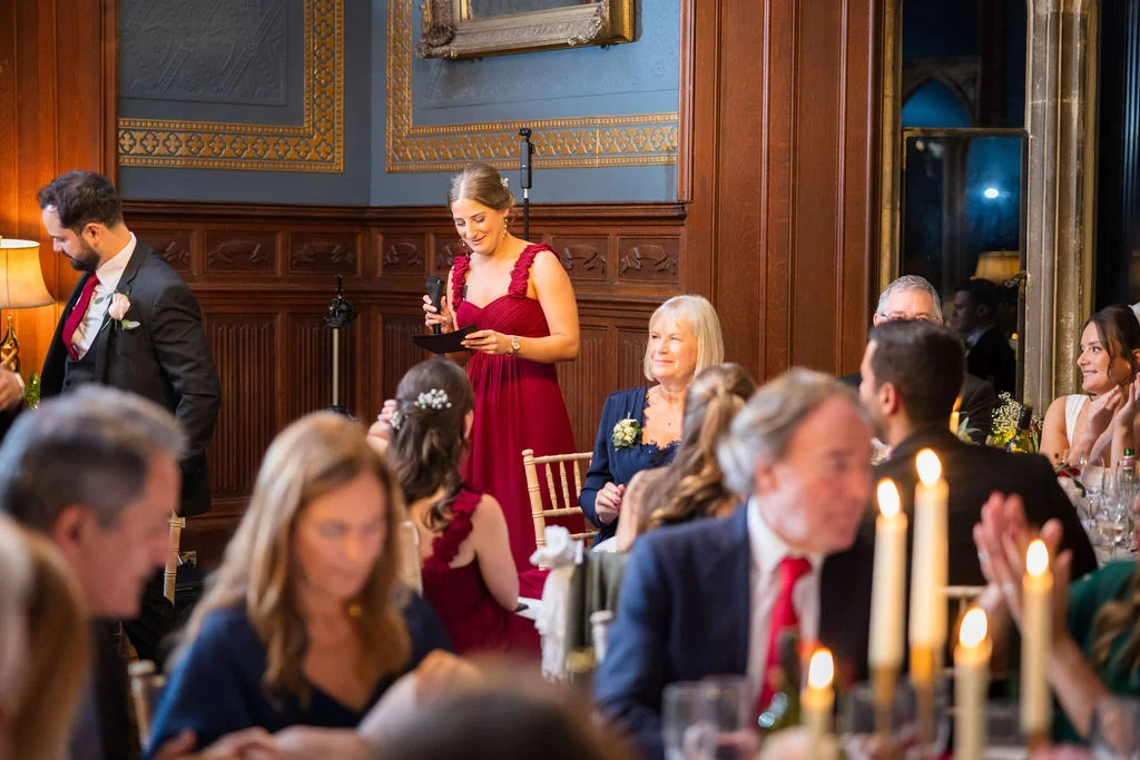 A bridesmaid gives a heartfelt speech during the wedding reception in a wood-panelled dining room lit by warm candlelight.
