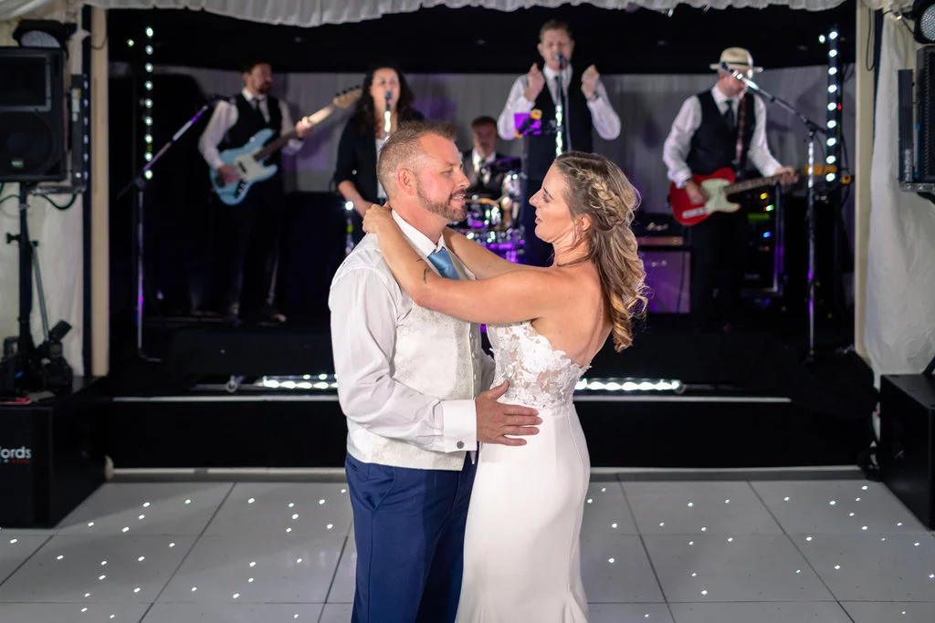 The newlywed couple share their first dance on a starlit dance floor while a live wedding band performs on stage behind them.