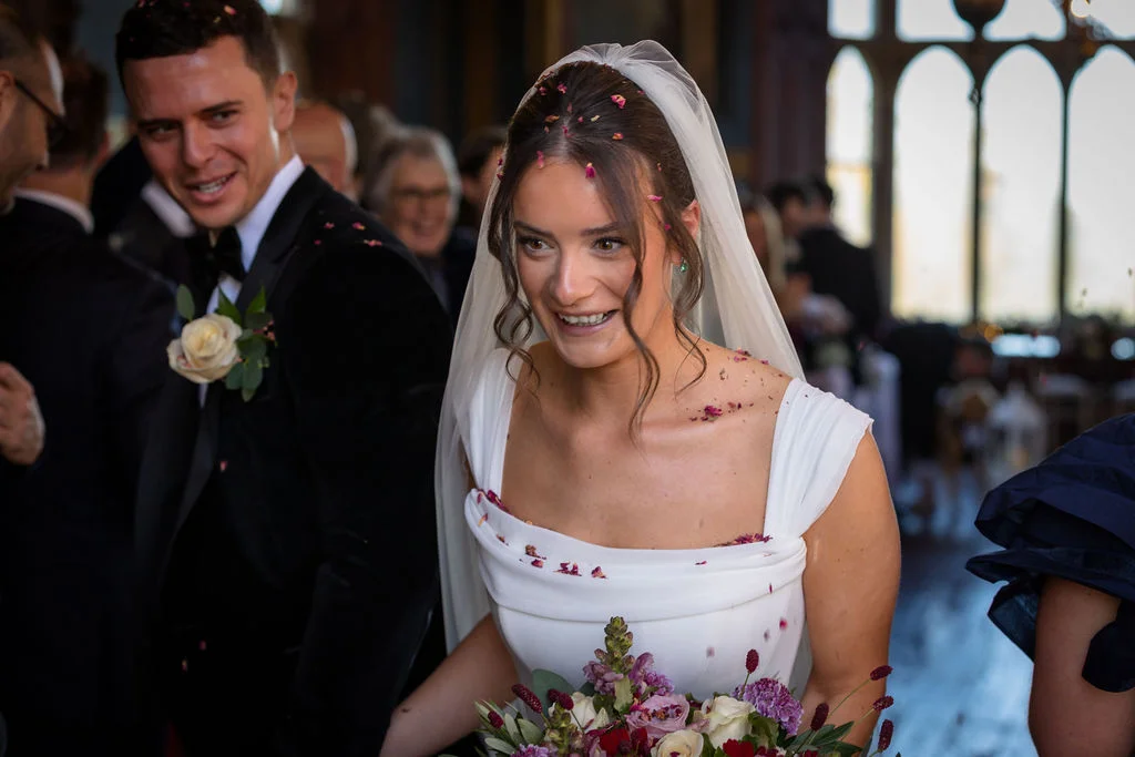A joyful newlywed couple smiles as they walk down the aisle during their church wedding ceremony amidst falling confetti petals.