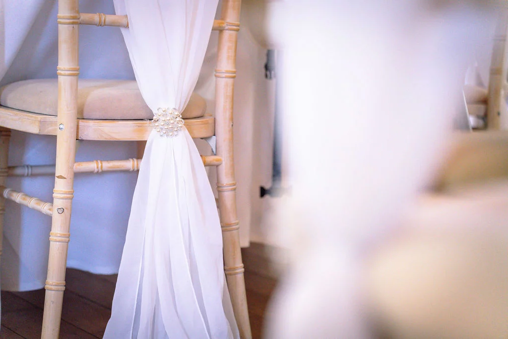 A wooden chiavari wedding chair is elegantly decorated with white chiffon fabric gathered at the back with a pearl and crystal brooch.