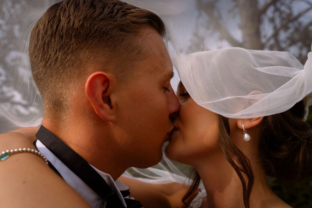 A bride and groom kissing in front of a tree.