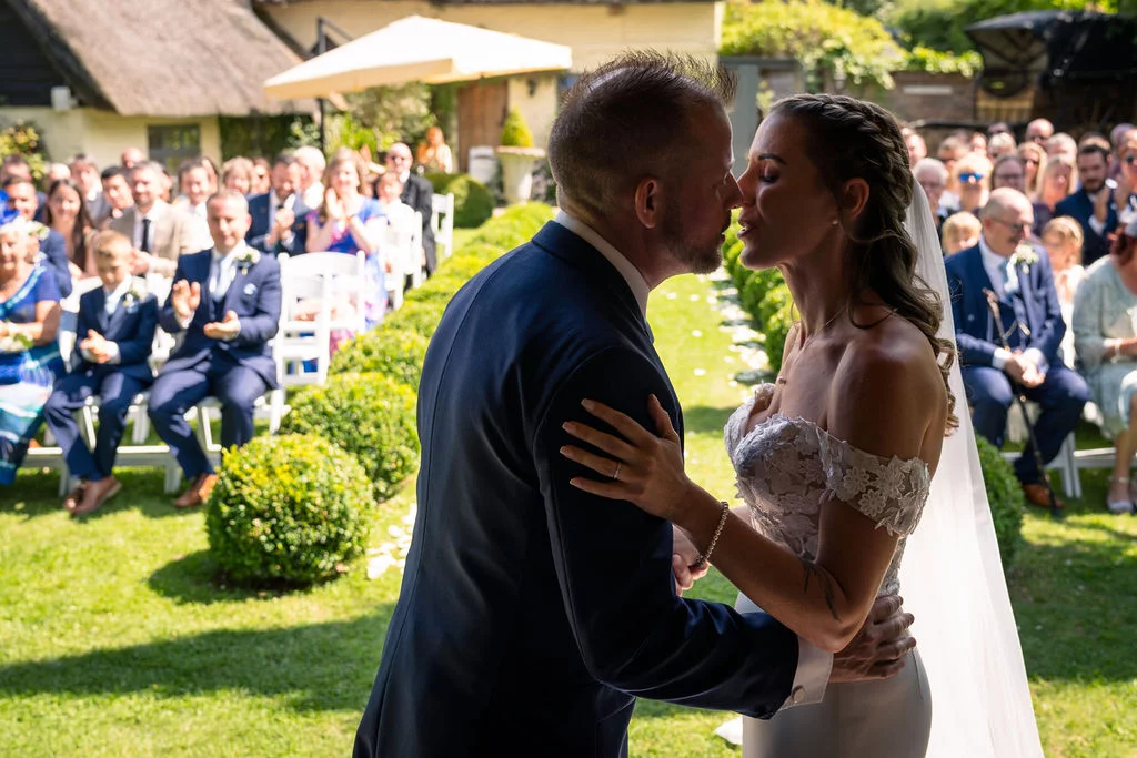 The newly married couple share their first kiss at the top of the aisle during an outdoor garden wedding ceremony.