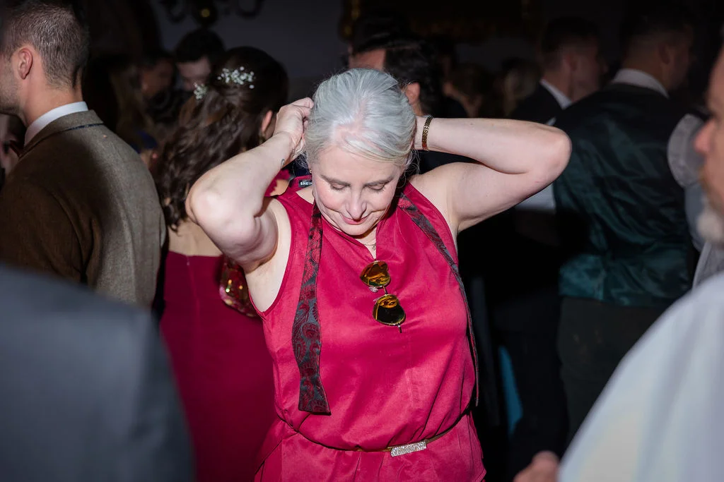 A mature wedding guest with grey hair adjusts her hair while wearing a red dress during an evening reception.