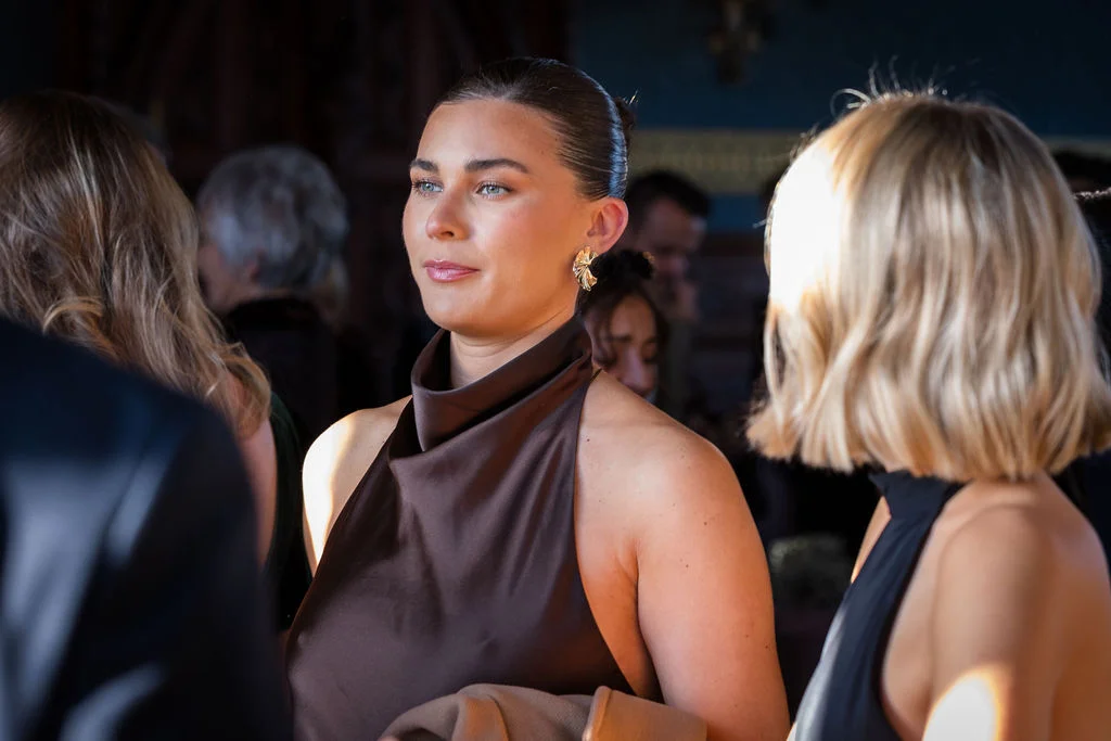 A guest with a sleek bun and statement earrings mingling at a wedding reception bathed in natural side light.