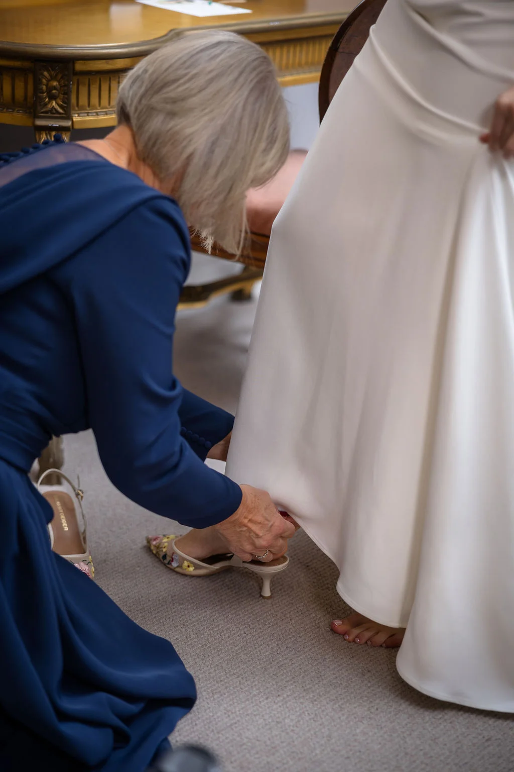A mother helping the bride with the finishing touches on her wedding dress during morning preparations.