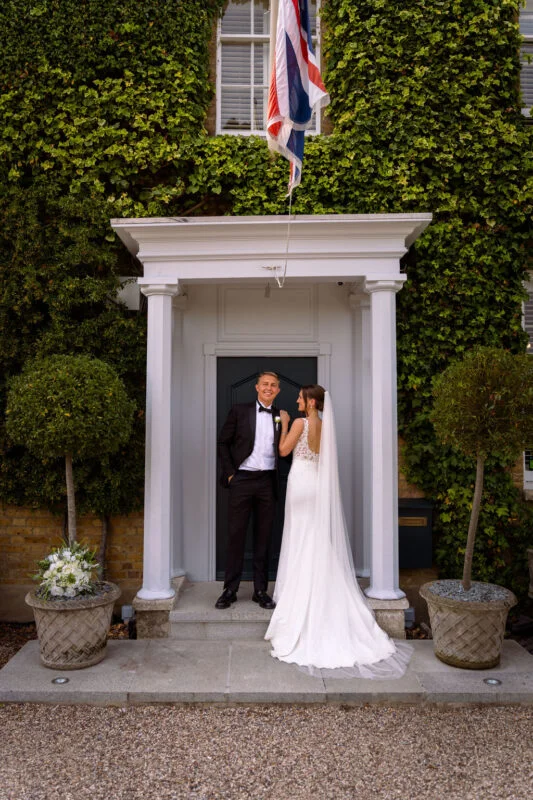 A bride and groom kissing in front of a house with a flag.