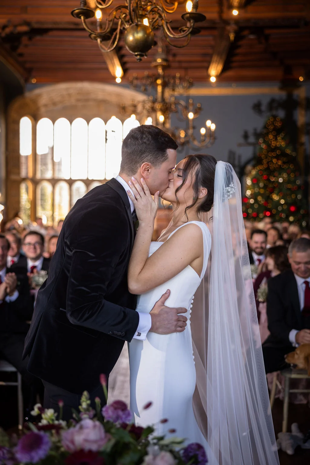 Newlyweds share their first kiss at the altar inside a historic hall decorated for a winter wedding.